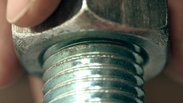 Hand is screwing a huge nut onto a large shiny metal screw with thread macro. 4K real time video. Bottom view