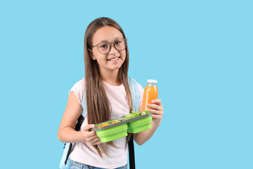 Happy little girl with bottle of juice and lunchbox on blue background