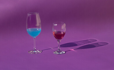 Minimal scene wine glass with red wine and blue cocktail on sunny day. Summer concept drinks and shadows on velvet background.