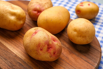 Wooden board with fresh raw potatoes on table, closeup