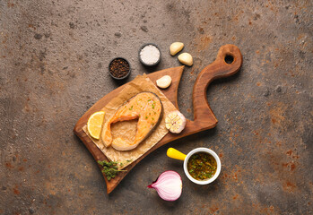 Wooden board of tasty salmon steak with garlic, onion and lemon on brown background