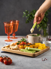 Mix of fresh vegetables on a wooden plate. Vegetarian snack. Pieces of pepper, celery with hummus on a menazhnitsa.