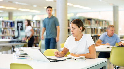 Portrait of young woman studying at library using books and laptop
