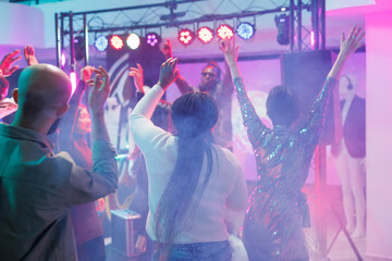 Energetic crowd dancing and enjoying discotheque on dancefloor with colorful spotlights. People...