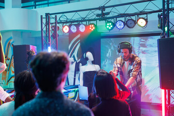 People attending techno music concert and enjoying nightlife in club illuminated with lights. Man...