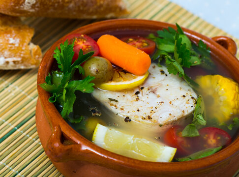 Fisher soup from merluccius. Recipe: boil broth from fish head, add potatoes, carrots, shallots, corn, fish fillets or steak 200 g, season with salt, pepper. Then cook in oven at 200 deg for 40min