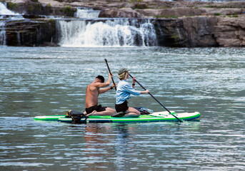 Couple on SUP boards in front of waterfall; Stand up Paddle Boards  