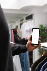 Customer in retail store using mobile phone empty white digital display while checking available apparel options. Shopping mall boutique client showing smartphone blank touchscreen