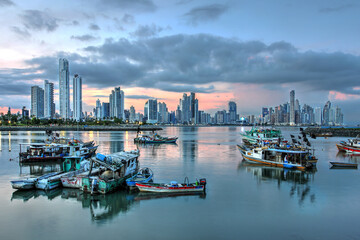 Futuristic skyline of Panama city at sunset against fishing boats reflecting in the still water.