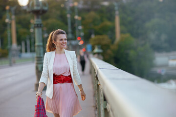 happy trendy woman in pink dress and white jacket in city