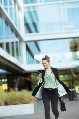 female employee in business district using phone and walking