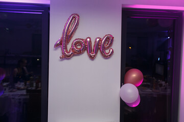Różowy napis LOVE na białej ścianie i kolorowe balony. Balon LOVE. Pink LOVE inscription on a white wall and colorful balloons. LOVE balloon.