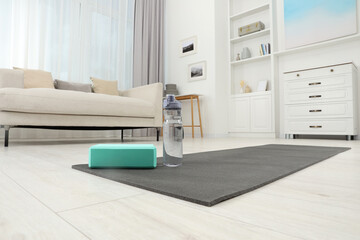 Exercise mat, yoga block and bottle of water on floor in room