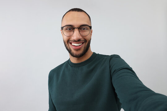 Smiling young man taking selfie on grey background