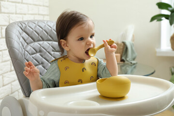 Cute little baby nibbling spoon in high chair indoors.