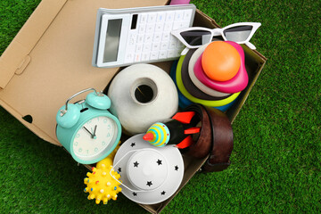 Box with different stuff on green grass, top view. Garage sale