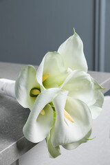 Beautiful calla lily flowers tied with ribbon on grey table, closeup