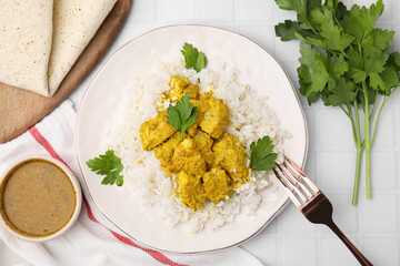 Delicious rice and chicken with curry sauce on white tiled table, flat lay