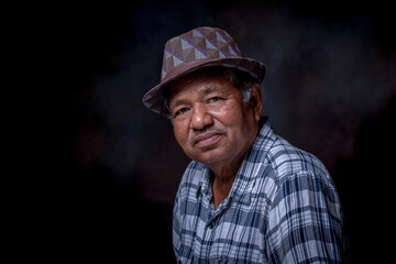 Portrait of senior man in his 60s wearing hat is looking at camera in studio with dark background.
