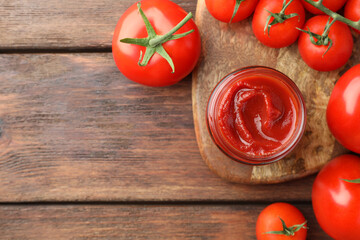 Jar of tasty ketchup and tomatoes on wooden table, flat lay. Space for text