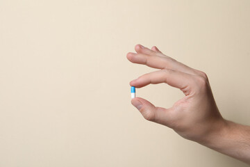 Man holding pill on beige background, closeup. Space for text