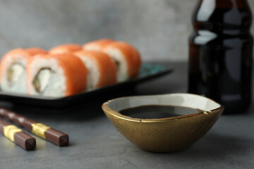 Tasty soy sauce, chopsticks and sushi rolls with salmon on grey table, closeup