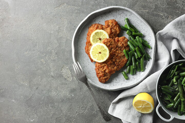 Tasty schnitzels served with lemon and green beans on grey table, flat lay. Space for text