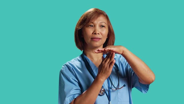 Close up shot of assertive asian nurse asking for timeout while at work. Clinic worker doing pause hand sign gesturing, wishing for break from job shift, isolated over studio background