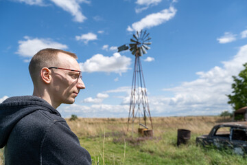 Jeune homme en extérieur près 'une voiture abandonné et d'une vieille éolienne © Esta Webster