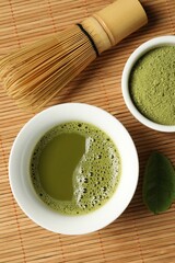Cup of fresh matcha tea, green powder and chasen on bamboo mat, flat lay