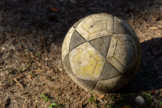 close da bola de futebol gasta e velha, iluminada por um raio de sol parada sobre o campo de terra da v&aacute;rzea