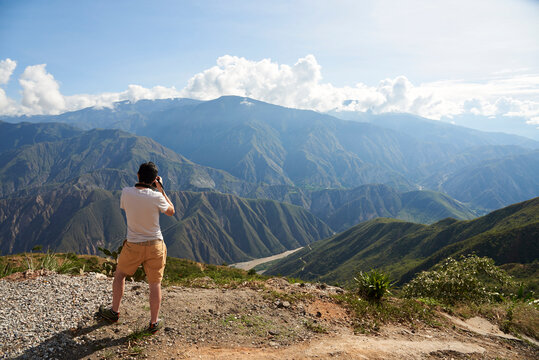 Unrecognizable young man seen from behind taking pictures of the Chicamocha Canyon, mountainous Andean scenery in Santander, Colombia under the morning sunlight.