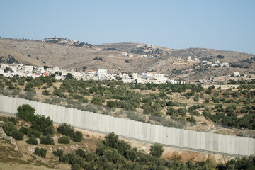 Fototapeta na wymiar A prefabricated concrete barrier passes along the Green Line, a border around the Judea and Samaria Area / West Bank, in Israel. A Palestinain village is on the hillside in the distance.
