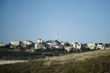 In the background, an Arab village on a hilltop has a mosque's minaret rising high. Next to the...
