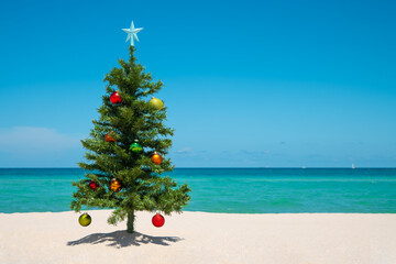 Christmas Tree on the beach. Merry Christmas. Happy New Year. Winter Holidays. Miami Florida vacation. Decorated Christmas pine or fir tree. Tropical Nature. Blue ocean on background with copy space