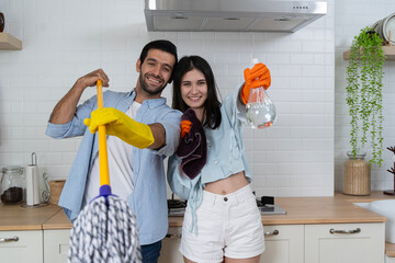 Handsome man holding mop and singing with woman while cleaning. Young couple cleaning up and...