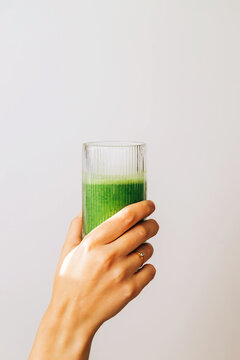 Close-up Of Female Hand Holding A Glass With Freshly Blended Green Smoothie Isolated Over White Wall, Healthy Lifestyle