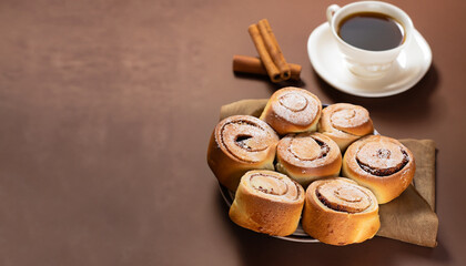 Rolls with cinnamon filling as well as a cup of coffee on brown background, Copy space
