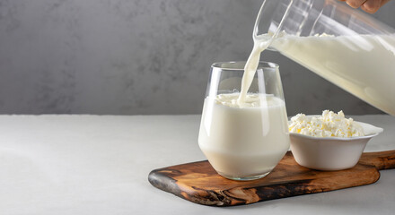 Kefir or Ayran fermented drink is poured into a glass from a jug, as well as cottage cheese in a...