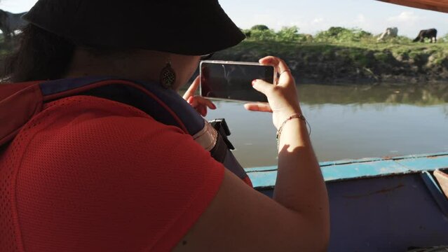 A Latina woman with a cellphone in her hand embarks on a serene adventure through the waters of the majestic Magdalena River in Mompox.