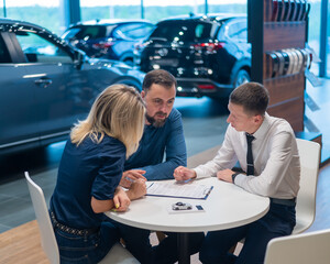 Happy caucasian couple signs a contract for the purchase of a car salon.