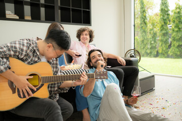 Multiethnic group of friends having fun playing guitar and singing together at home