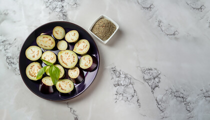 Eggplant cut into quarters for salad, placed in a plate on a marble background. On the table is a container with salt. View from above. Copy space