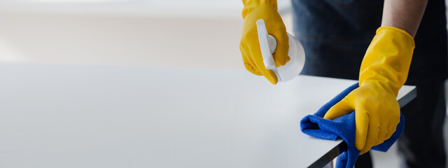 Person cleaning the room, cleaning staff is using cloth and spraying disinfectant to wipe the tables in the company office room. Cleaning staff. Maintaining cleanliness in the organization.