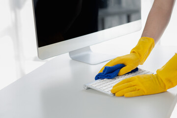 Person cleaning room, cleaning worker is using cloth to wipe computer keyboard in company office...