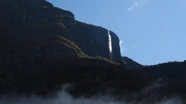 View of a dark mountain range with a sun lit waterfall