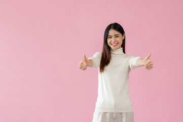 A beautiful Asian woman shows her thumbs up and stands against an isolated pink background