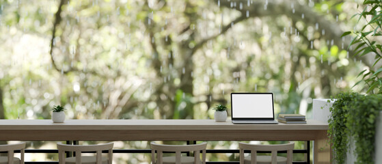 A laptop on a tabletop on a balcony or terrace with a beautiful nature view on a rainy day.