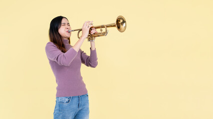 A beautiful and talented Asian woman is playing the trumpet, isolated yellow studio background