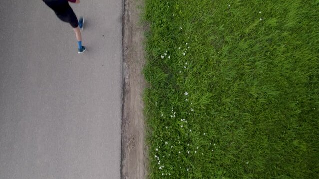 Aerial bird's eye view of man running and checking watch on asphalt path